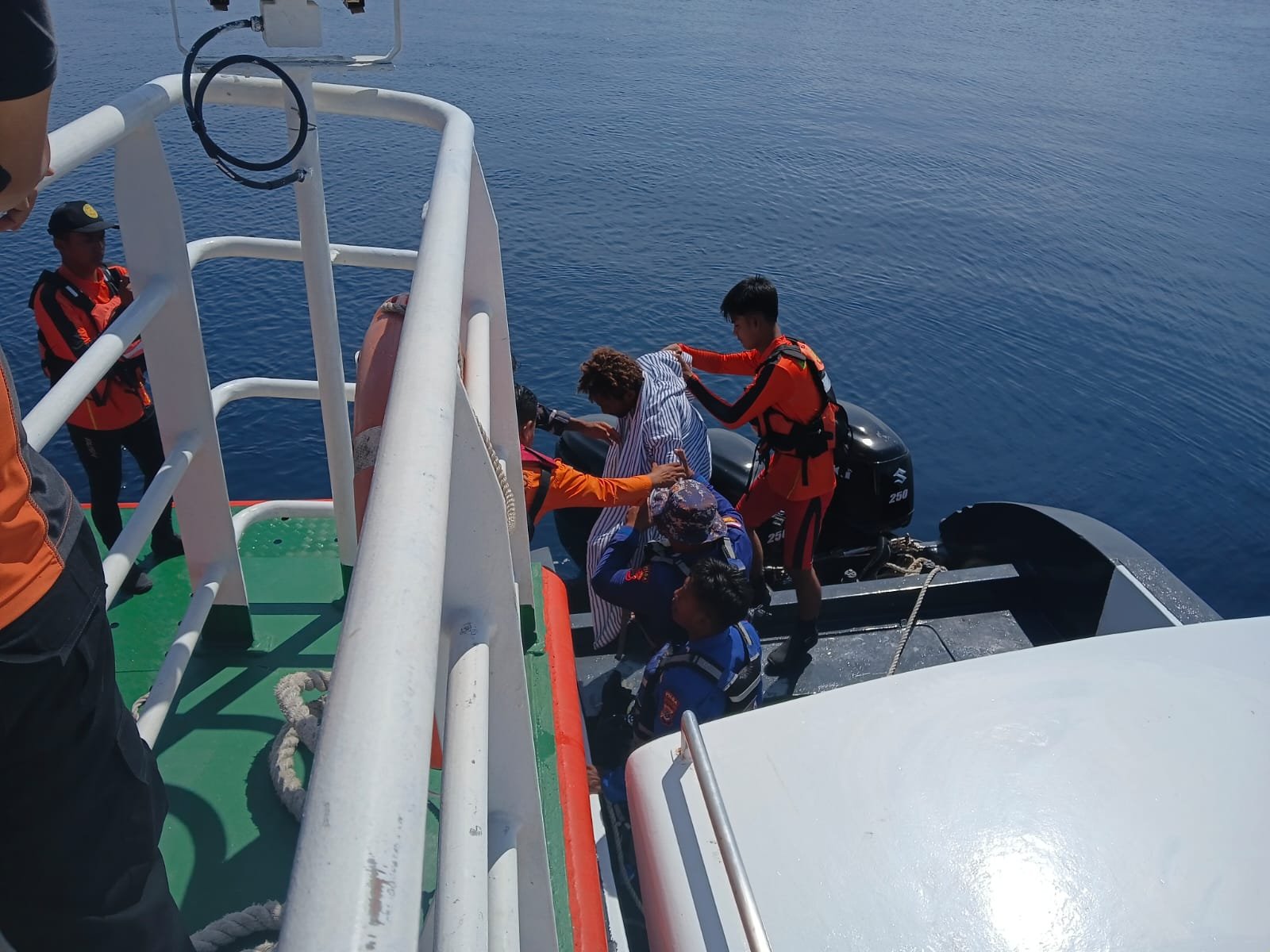 Rescue personnel assisting a diver between boats in Maumere Bay